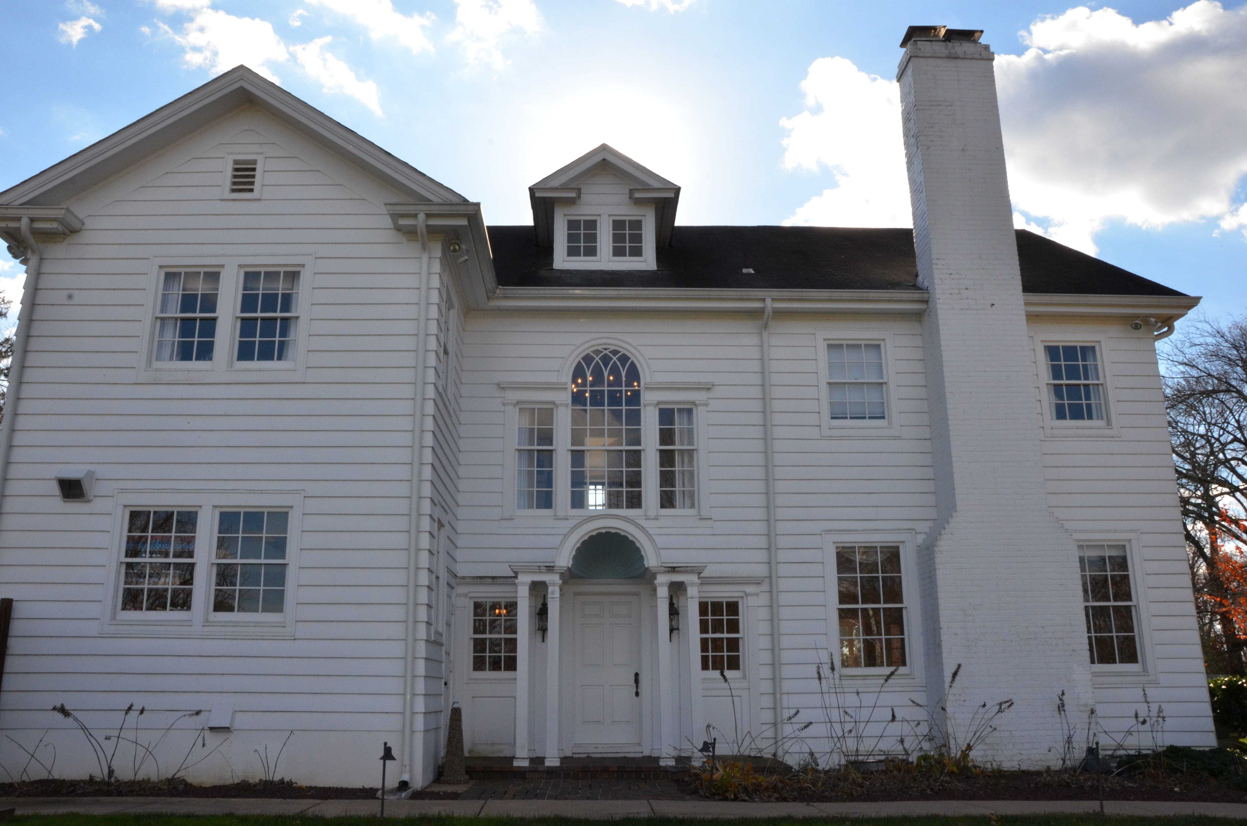 The front of a large white manor with blue sky and clouds in the background.